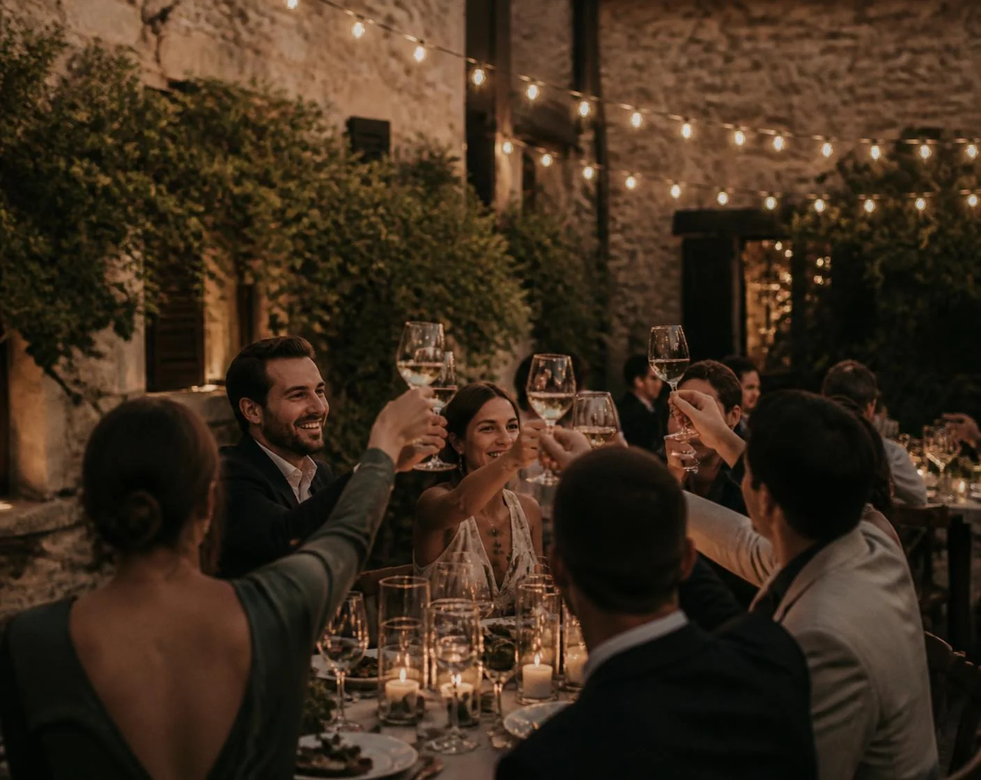 Guests toasting at a candlelit courtyard dinner under string lights