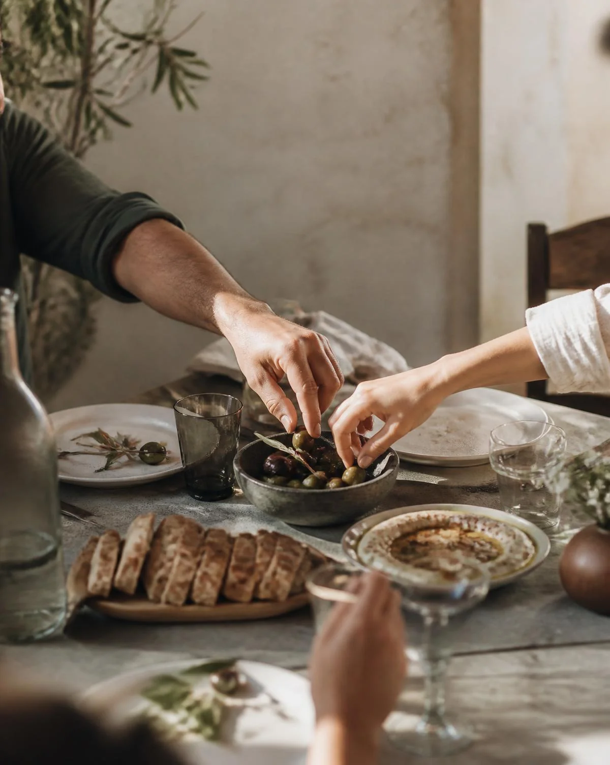 Hands reaching across a table of shared food in soft daylight